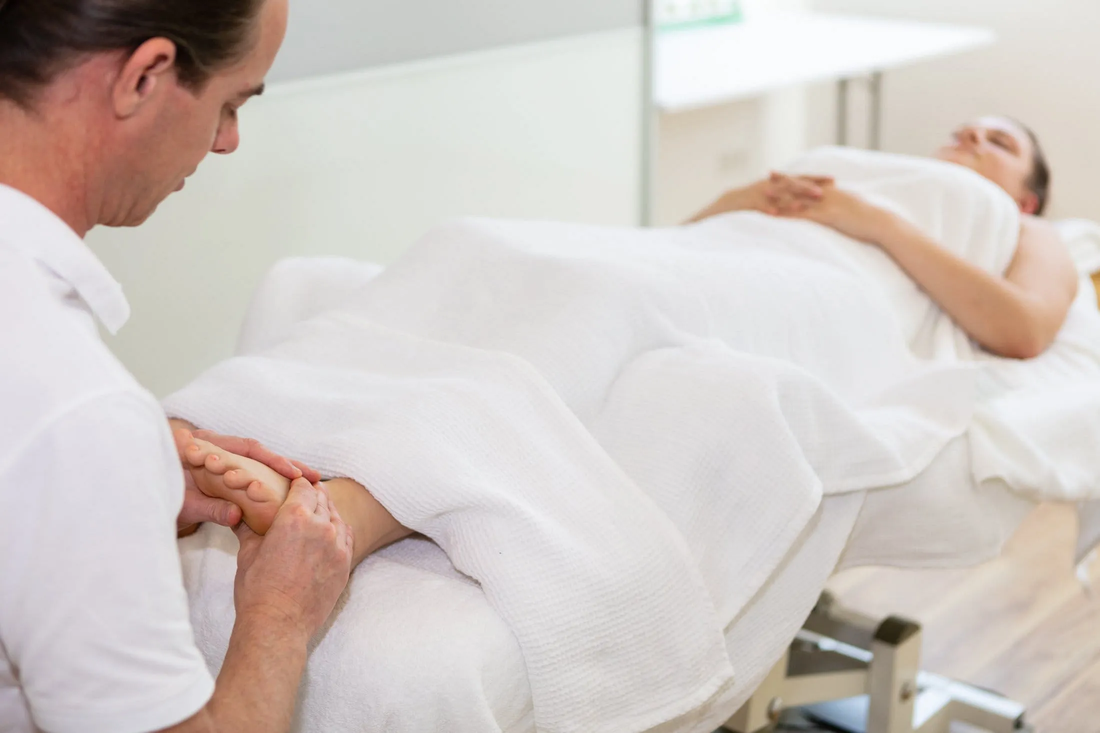 René Kricker behandelt den Fuß einer Patientin auf der Therapieliege